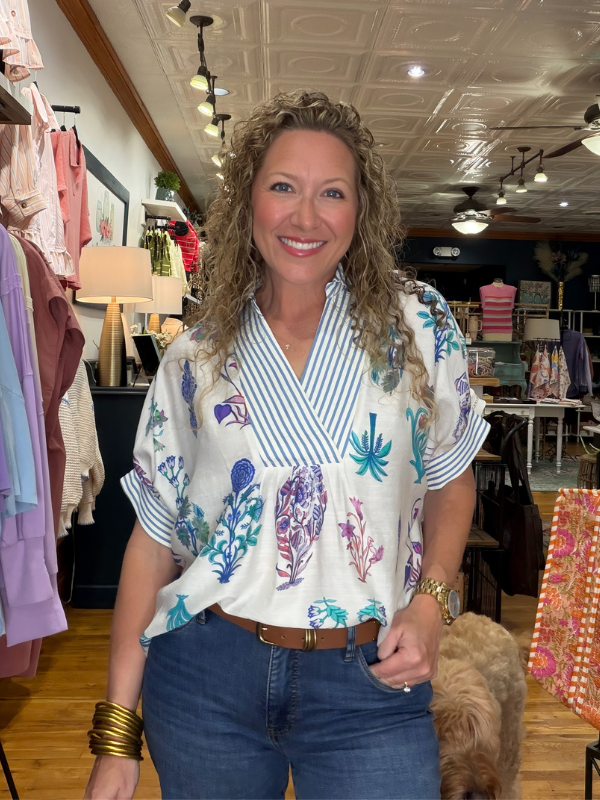 Woman in a colorful blouse and jeans standing in a store with a dog.