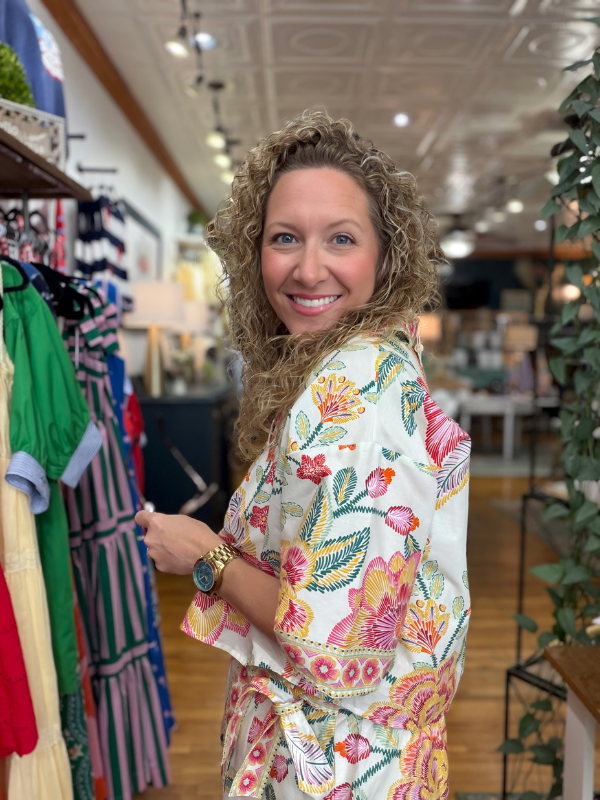 Woman in a floral kimono standing in a clothing store with racks of clothes in the background.