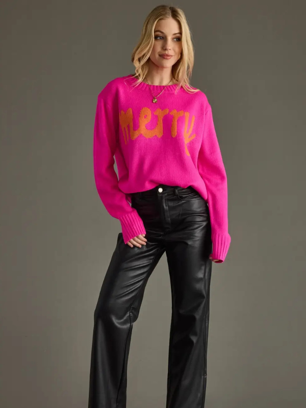 Person wearing a bright pink sweater with yellow text and black pants on a gray background