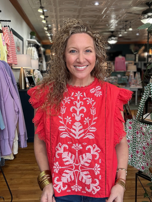 Woman wearing a red embroidered top in a store setting
