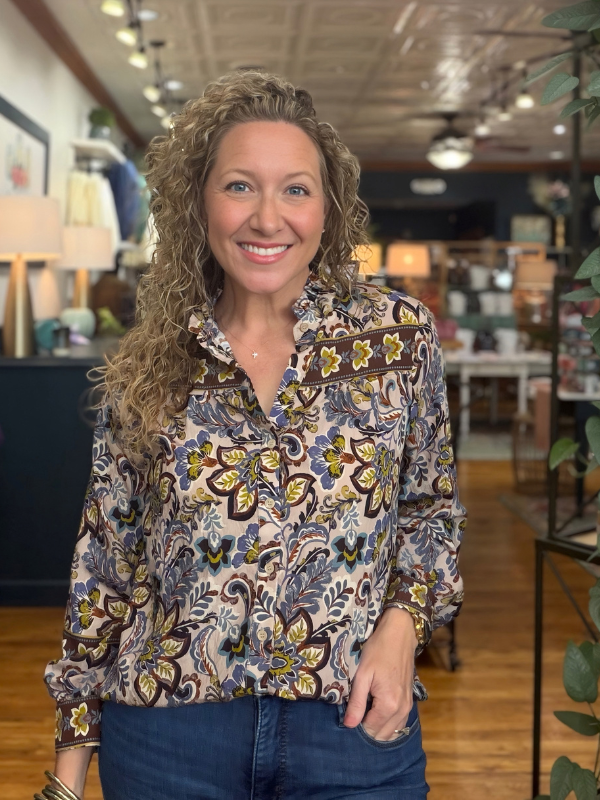 A woman modeling a long-sleeve high-neck blouse with a colorful floral and paisley print, paired with blue jeans