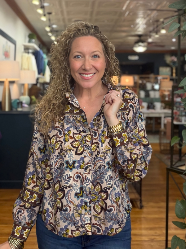 A woman modeling a long-sleeve high-neck blouse with a colorful floral and paisley print, paired with blue jeans