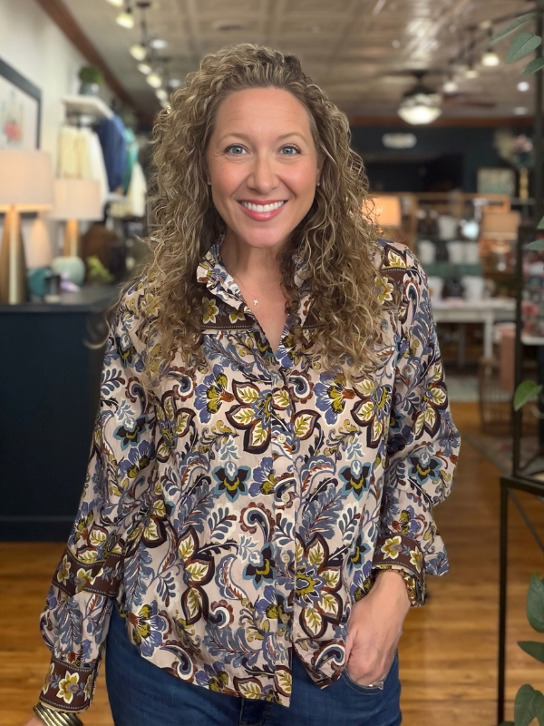 A woman modeling a long-sleeve high-neck blouse with a colorful floral and paisley print, paired with blue jeans