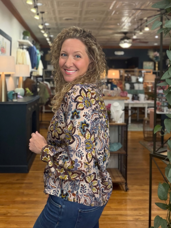 A woman modeling a long-sleeve high-neck blouse with a colorful floral and paisley print, paired with blue jeans