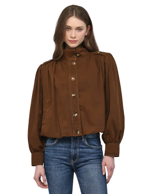 A woman modeling a cropped brown jacket with a high mock neck, gold-tone buttons, and voluminous long sleeves, paired with blue jeans against a plain white background.