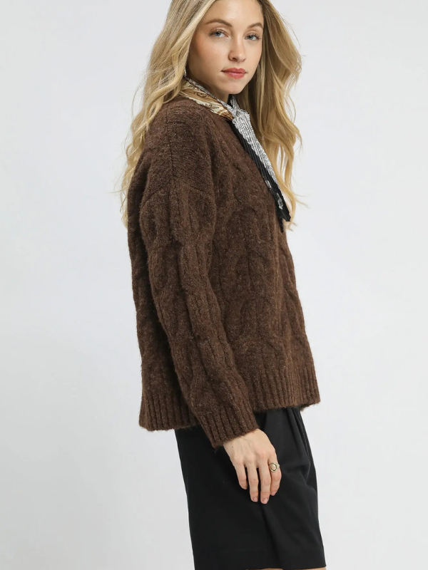 Woman wearing a brown cable knit sweater on a white background