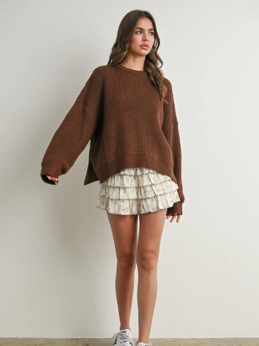 Woman wearing a brown sweater and patterned skirt against a plain background