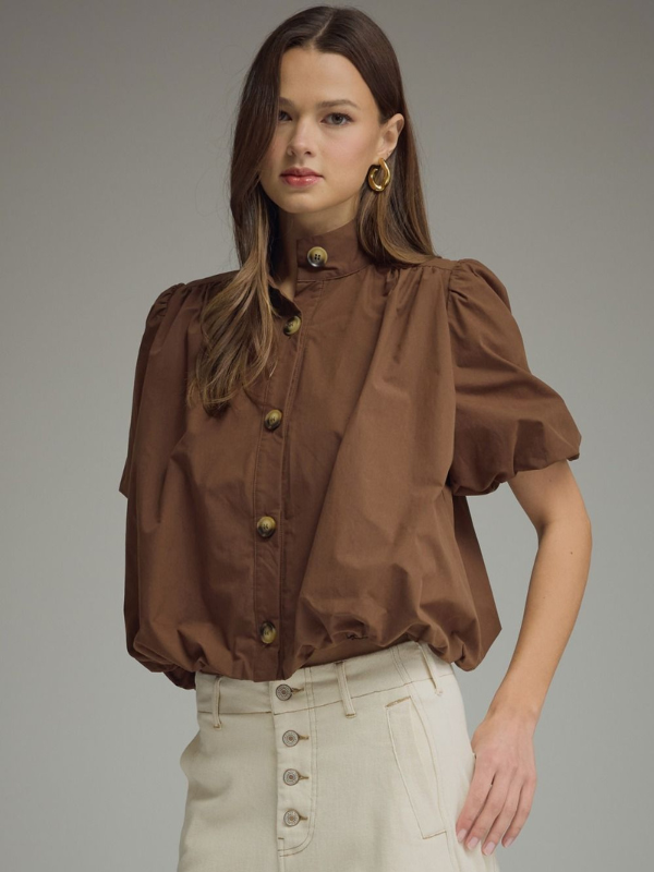 Woman wearing a brown blouse with puff sleeves against a gray background