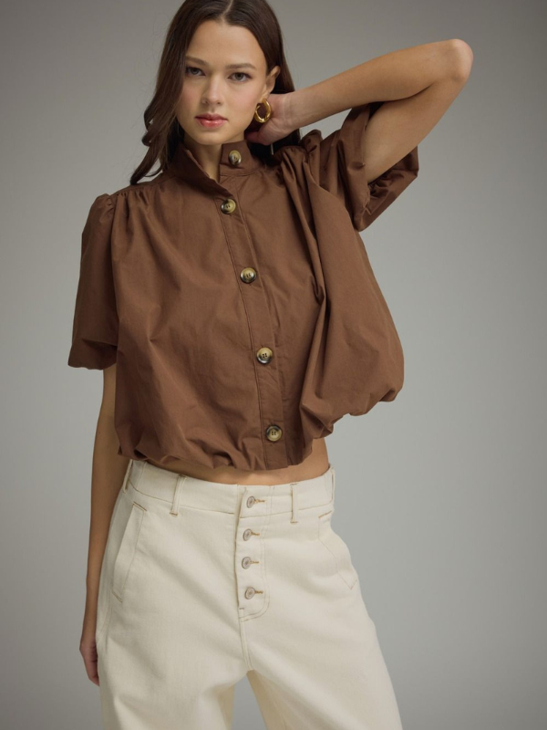 Woman wearing a brown blouse with puff sleeves and beige pants on a gray background