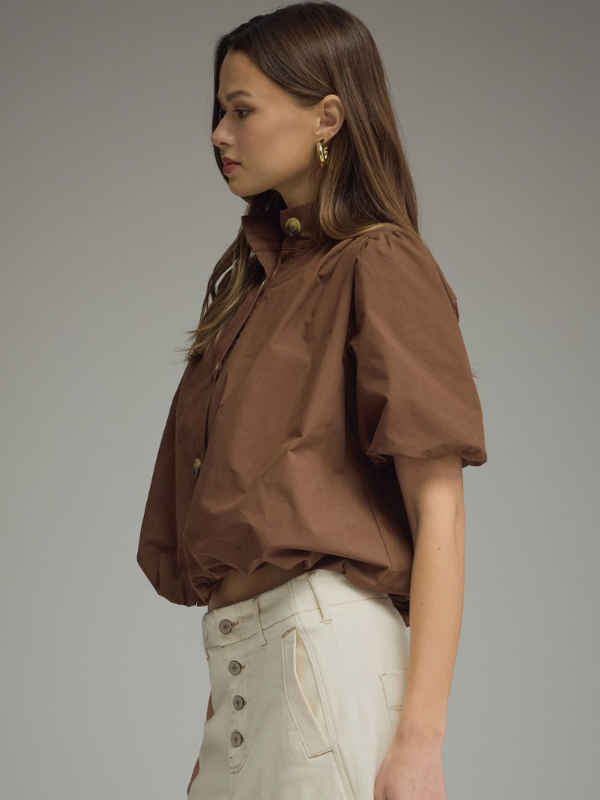 Woman wearing a brown blouse and beige pants against a plain background