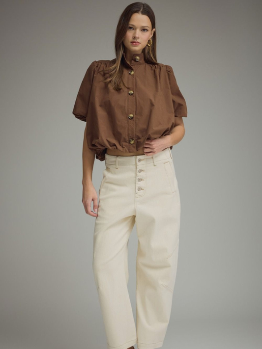 Woman wearing a brown blouse and beige pants against a gray background