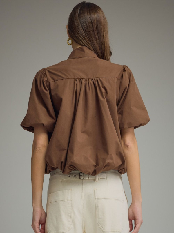 Person wearing a brown blouse with puff sleeves on a gray background