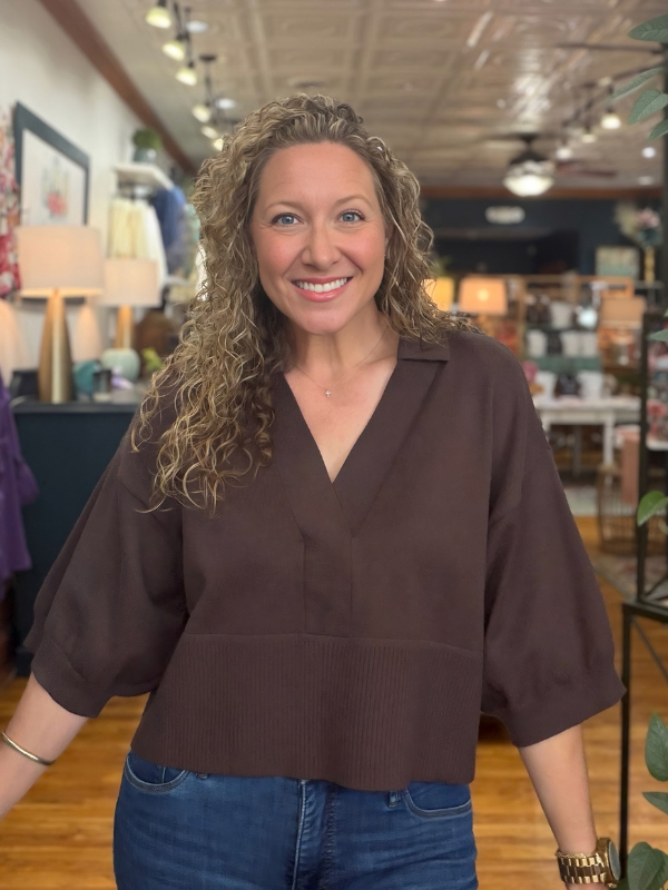 A woman wearing a dark brown knit polo sweater with jeans
