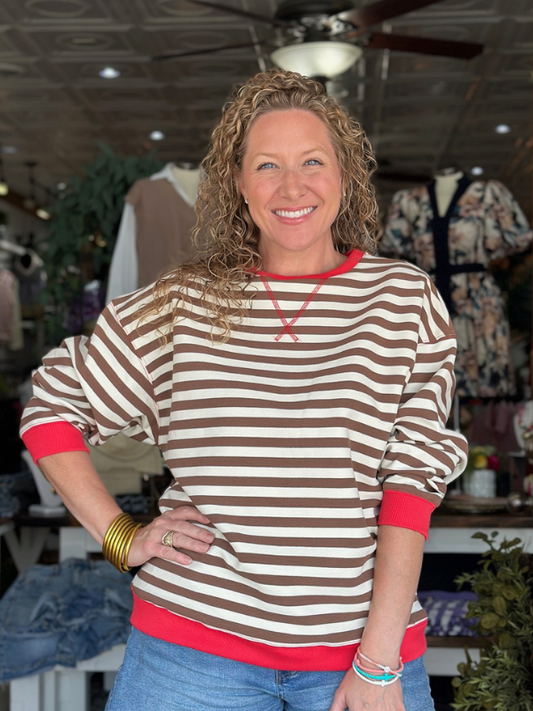 Woman wearing a brown and beige striped sweater with red trim in a store setting.