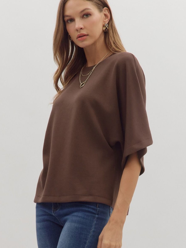 Woman wearing a brown oversized shirt and blue jeans on a plain background