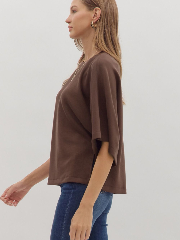 Woman wearing a brown oversized t-shirt and blue jeans on a plain background