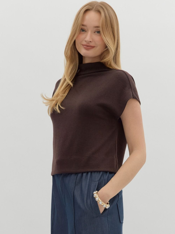 Woman wearing a brown turtleneck top and blue pants on a plain background