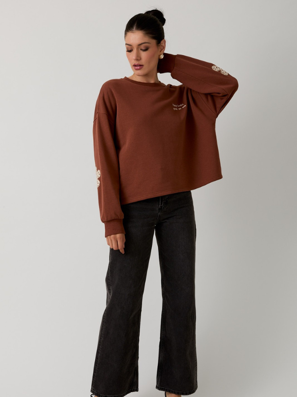 Woman wearing a brown sweatshirt and black pants on a plain background