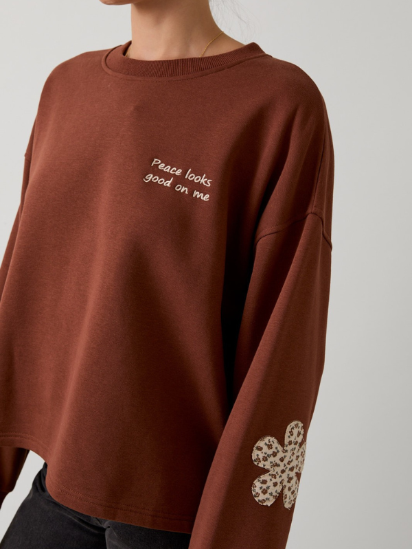 Brown sweatshirt with text and floral design on a plain background