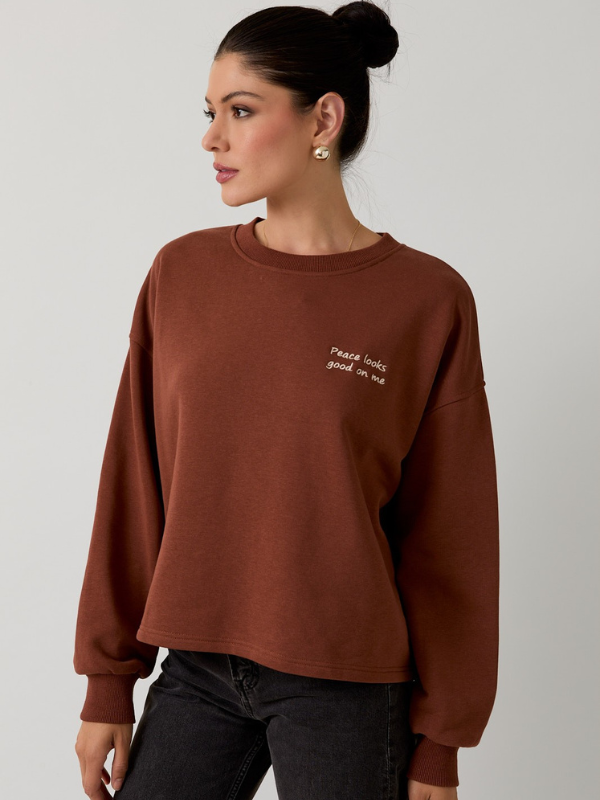 Woman wearing a brown sweatshirt with text on a plain background