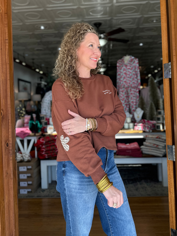 Woman wearing a brown sweatshirt with a logo and blue jeans standing in a store.