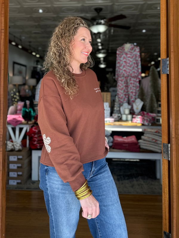 Woman in a brown sweatshirt and blue jeans standing in a store.
