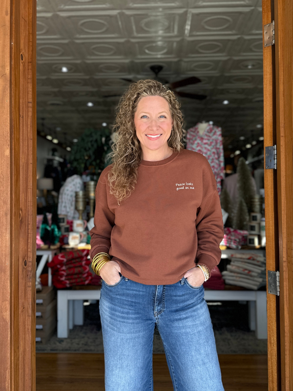 Woman wearing a brown sweatshirt with text, standing inside a store.