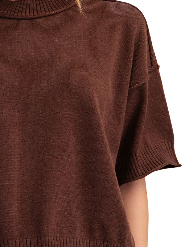 Close-up of a brown ribbed knit short-sleeve top worn by a model, showing the shoulder, sleeve cuff, and part of the arm against a white background.
