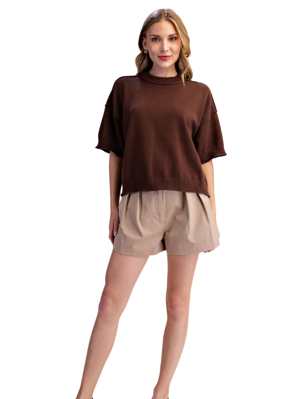 A woman modeling a brown short-sleeve knit sweater and beige shorts against a plain white background.