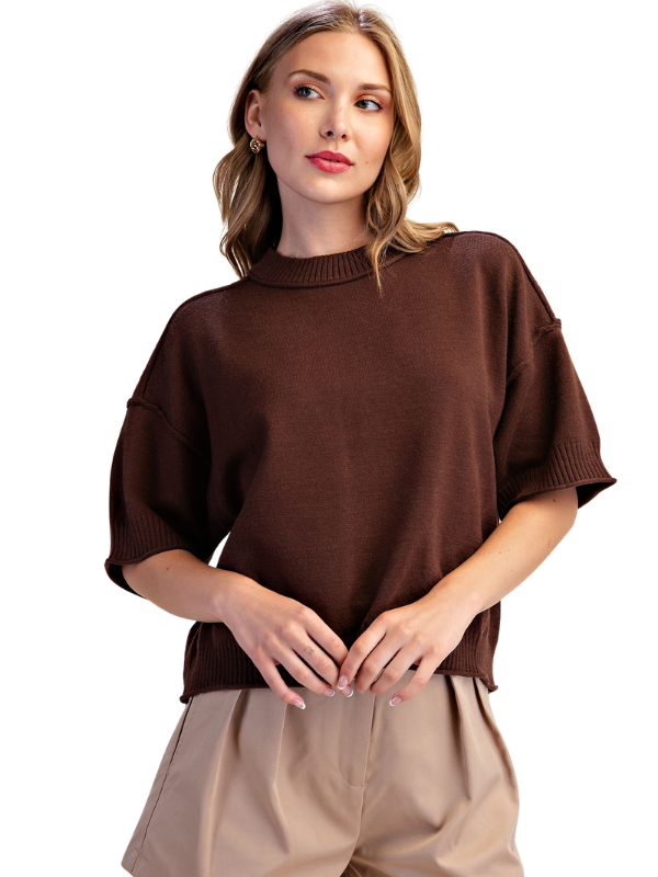 A woman wearing a dark brown short-sleeve knit sweater and beige pants, photographed against a plain white background.