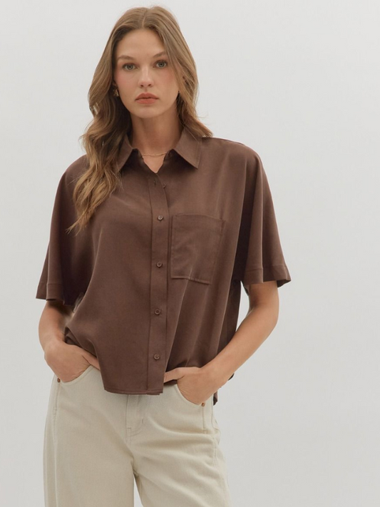 Woman wearing a brown shirt and beige pants against a plain background