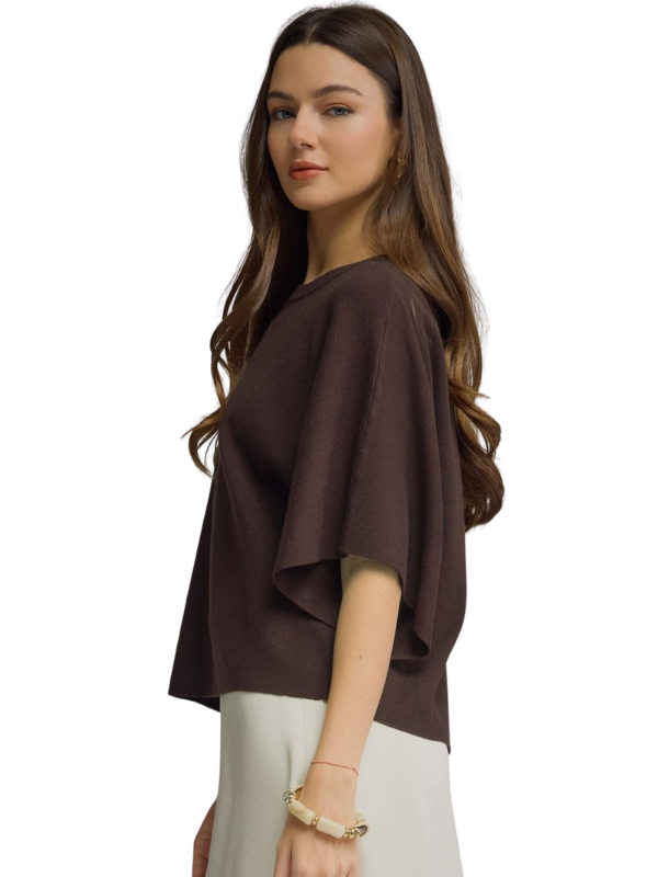 A woman wearing a dark brown draped short-sleeve top and light beige pants, shown from a side profile against a plain white background.