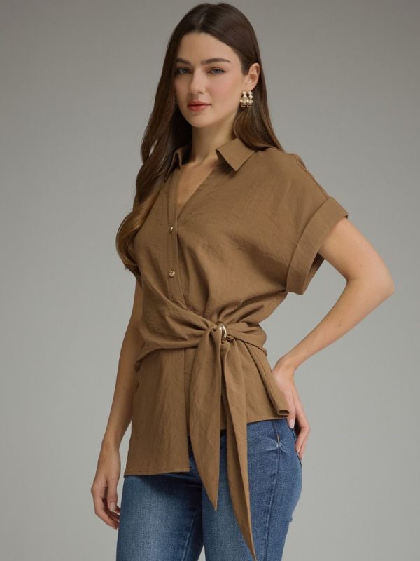 A woman modeling a brown short-sleeve wrap-style blouse with a tie waist, paired with blue jeans, against a plain gray studio background.
