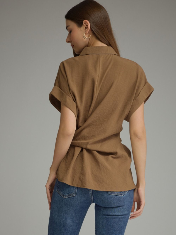 A woman shown from the back wearing a brown short-sleeve wrap-style blouse and blue jeans against a plain gray studio background.