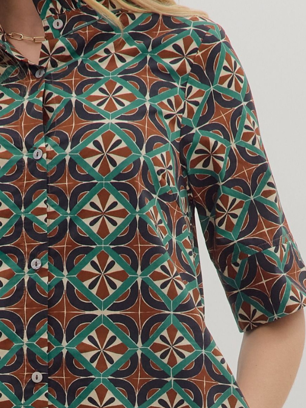 Close-up of a patterned shirt with geometric design in green, brown, and black on a plain background.
