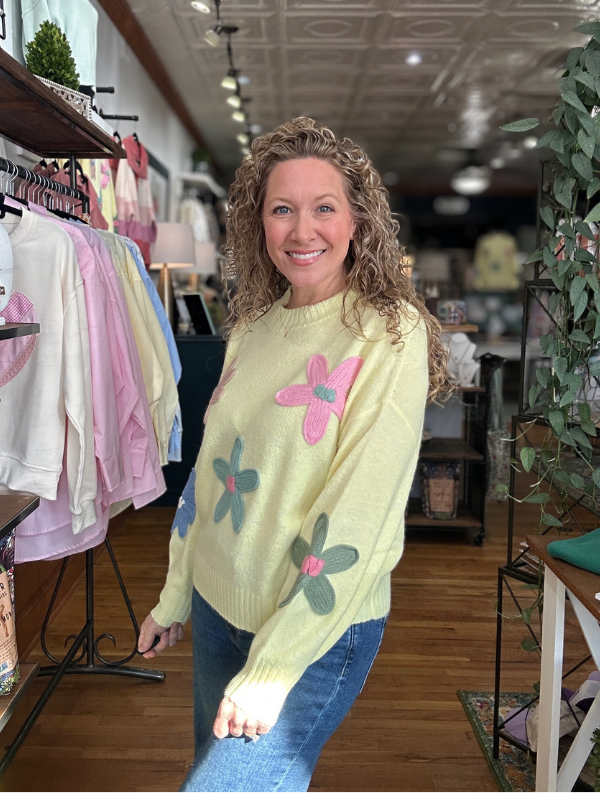 Woman wearing a light yellow sweater with floral designs in a clothing store.