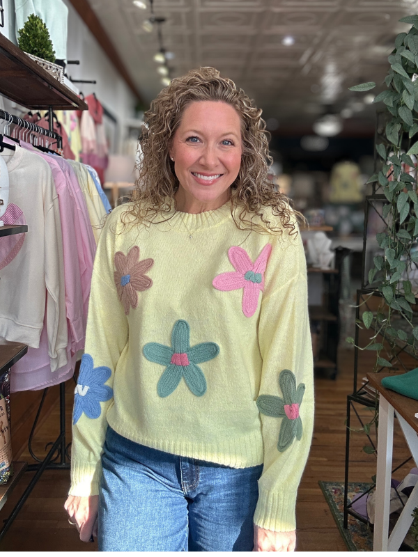 Woman wearing a light yellow sweater with colorful flower patterns in a store setting.
