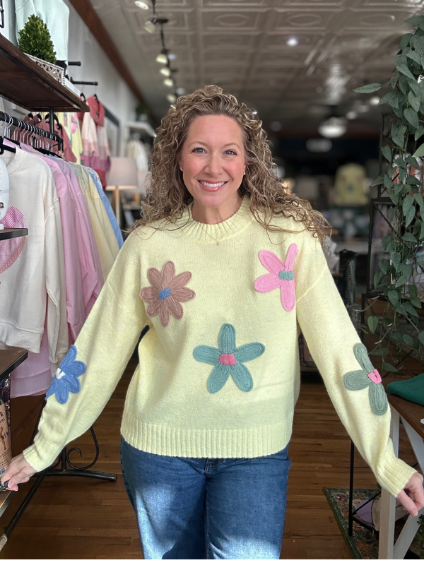 Woman wearing a light yellow sweater with colorful flower patterns in a store setting.
