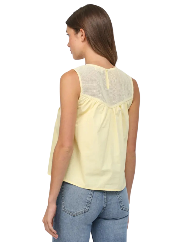 Woman wearing a light yellow sleeveless top and blue jeans on a white background
