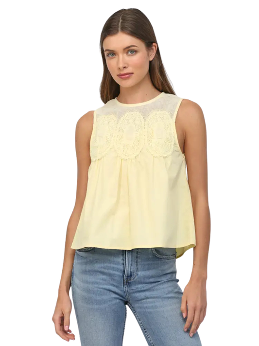 Woman wearing a light yellow sleeveless top with lace details and blue jeans on a white background