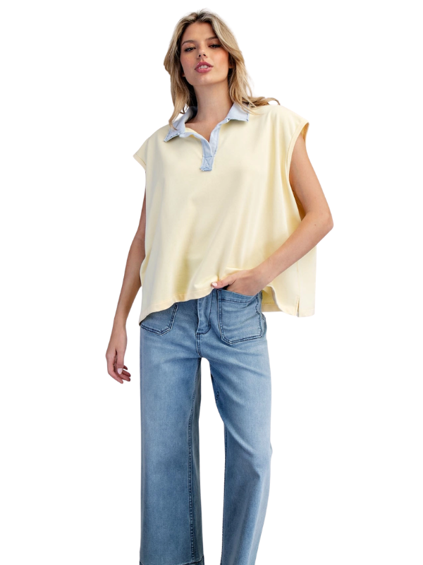 Woman wearing a yellow sleeveless top with a blue collar and light blue jeans on a white background