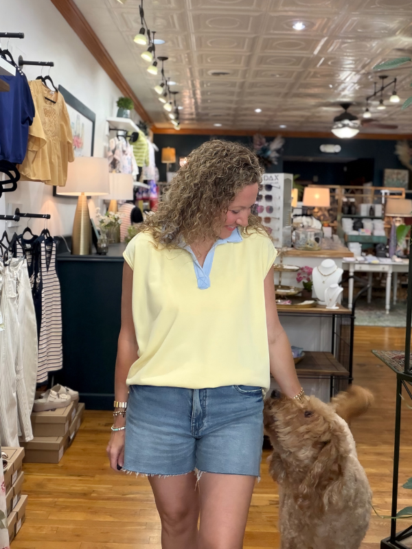 Woman in a yellow top and denim shorts standing with a dog in a store.