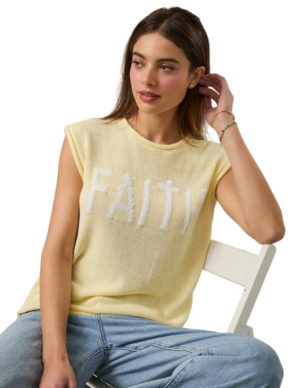 Woman wearing a yellow 'FAITH' t-shirt sitting on a white chair.