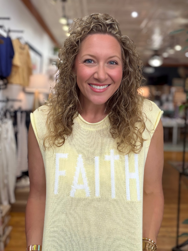 Woman wearing a yellow sleeveless shirt with 'FAITH' printed on it in a store setting.