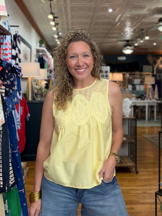 Woman wearing a yellow top and blue jeans standing in a store with clothing racks and displays.