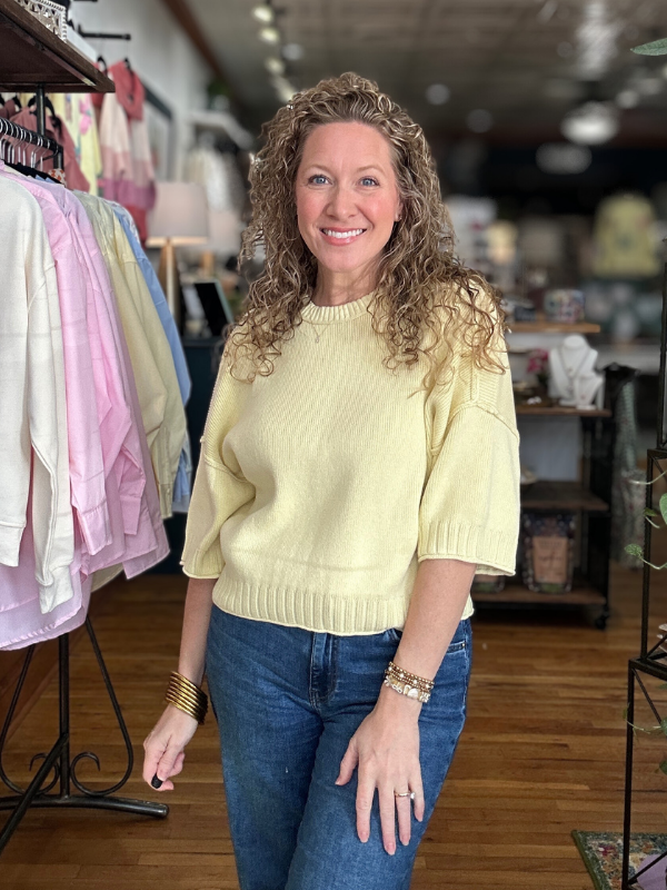 Woman wearing a light yellow sweater and blue jeans in a store setting