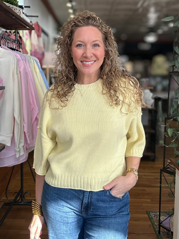 Woman wearing a yellow sweater and blue jeans standing in a clothing store.
