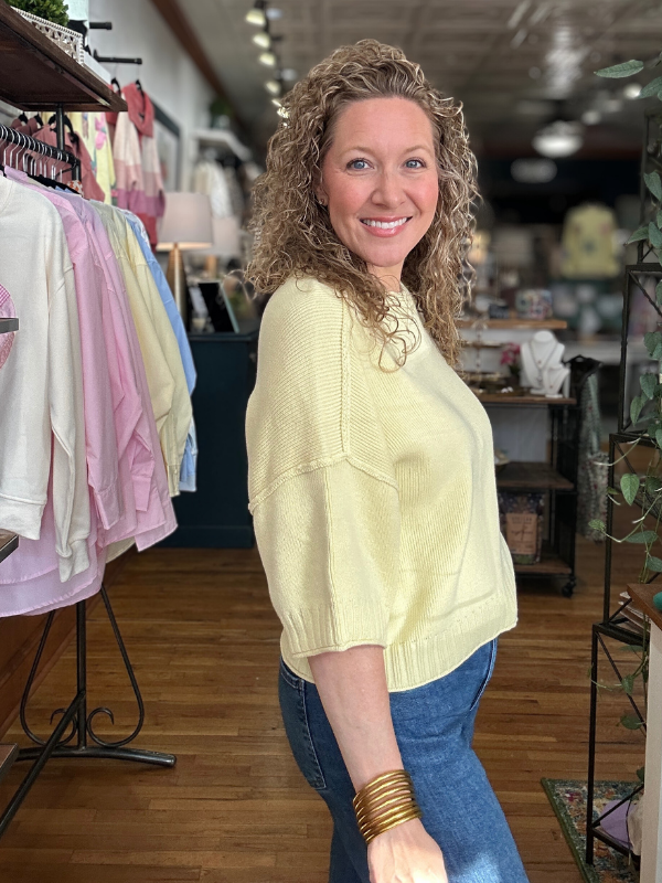 Woman in a yellow sweater standing in a store with clothing racks in the background