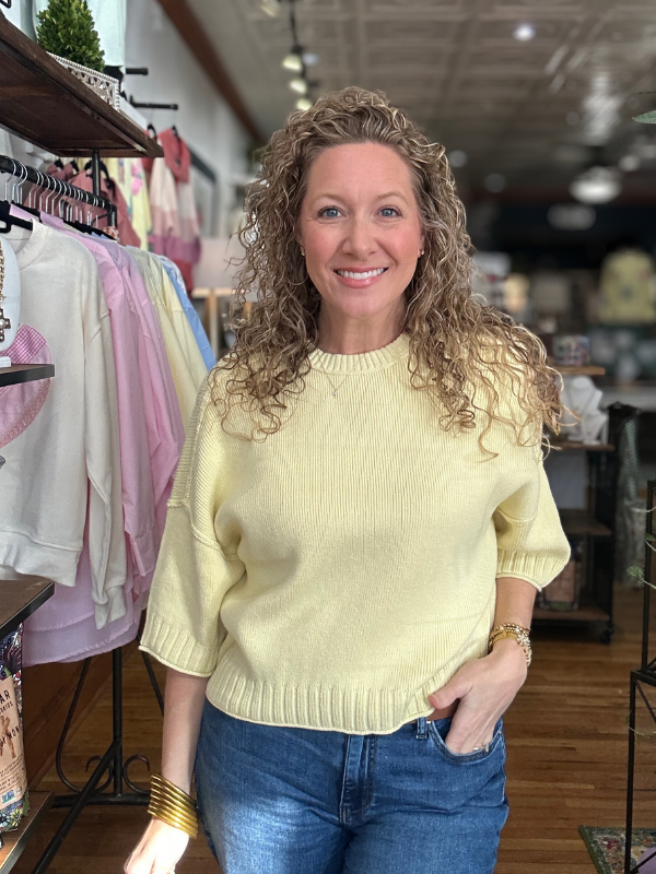 Woman wearing a yellow sweater and blue jeans in a store setting