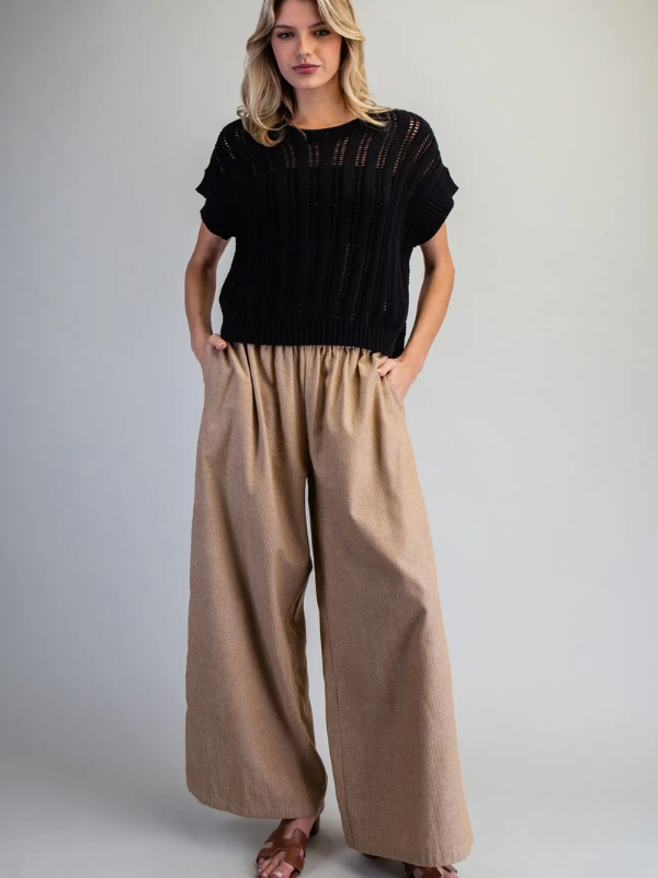 Woman wearing a black top and beige wide-leg pants on a plain background